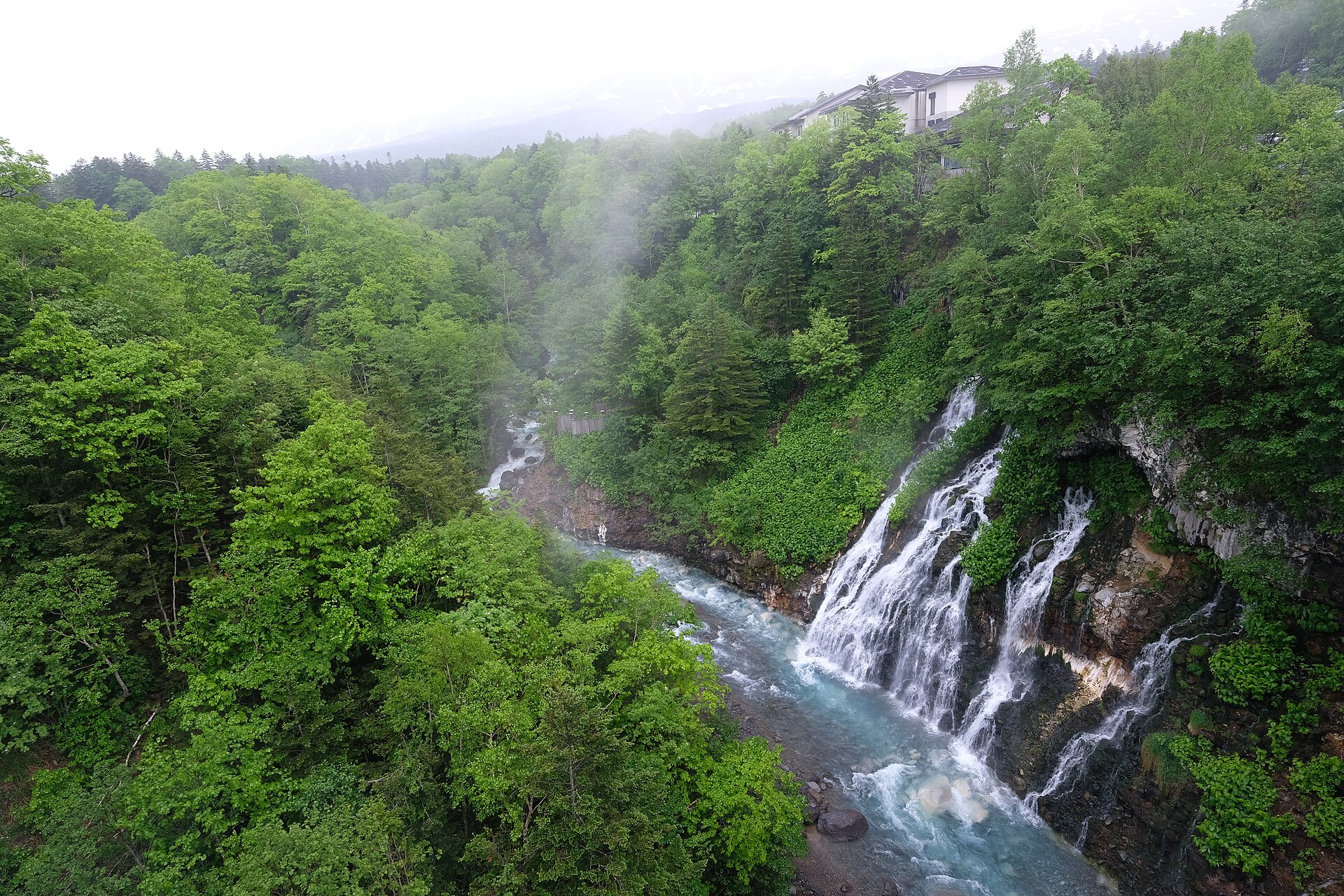 岩の割れ目から幾筋も落ちる白ひげの滝と青く濁る美瑛川
