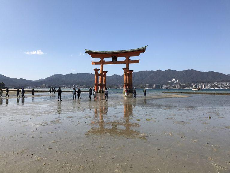干潮で潮が引いた砂州に立つ嚴島神社の大鳥居と、その根元まで歩いて近づく人々